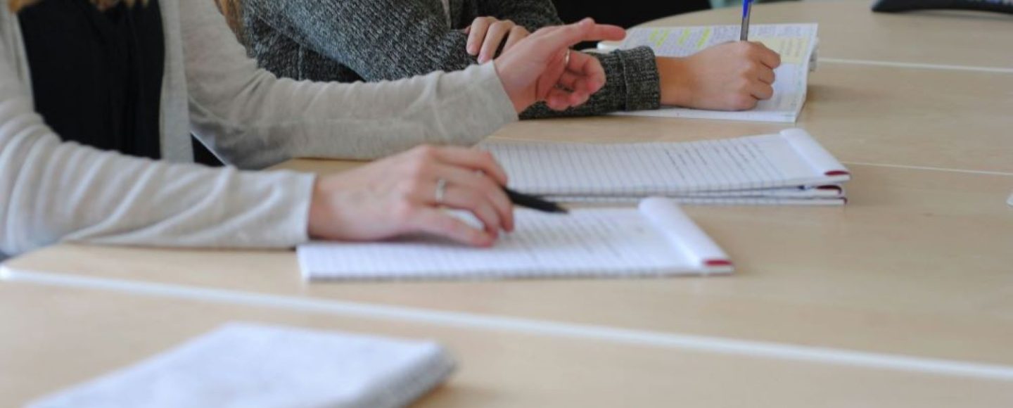 Nuoret pöydän ääressä. Pöydällä on vihkoja, joihin nuoret kirjoittavat.