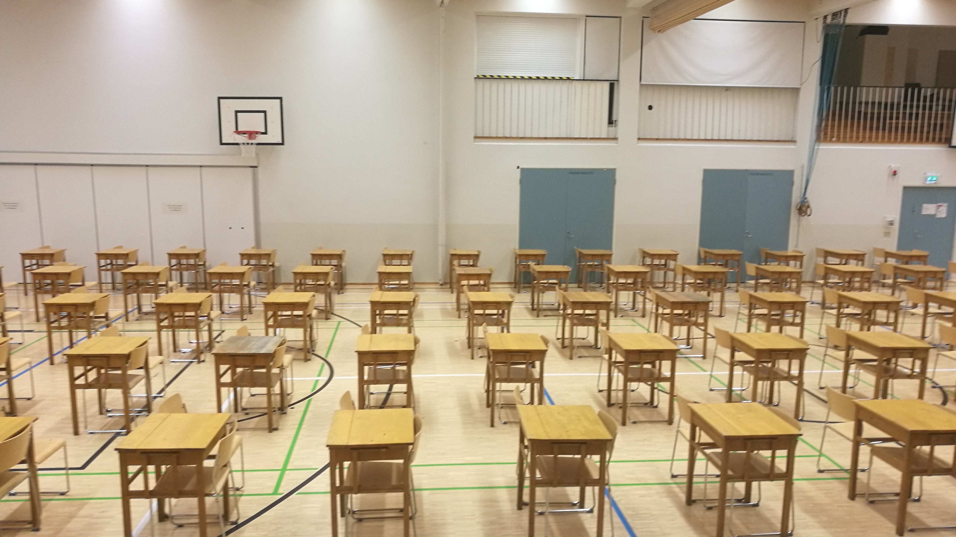 Koulun liikuntasalissa toisistaan erillisiä tyhjiä pulpetteja ylioppilaskirjoituksia varten.