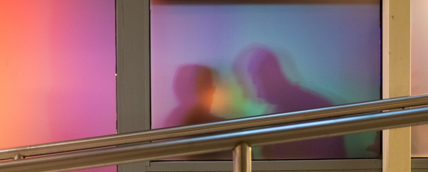 An abstract illustrative image for the article on inclusivity in urban planning. The silhouettes of the heads of two humans are seen through a frosted glass window. In front of the windows there is a handrail made of metal.
