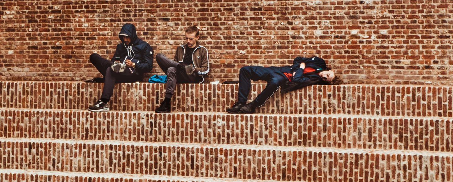 punaisenruskealla tiiliportaikolla istuu ja makoilee kolme nuorta miestä